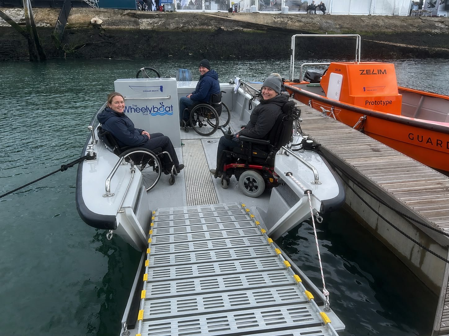 Main About Us Image: Wheelchair users boarding BoatHub's accessible vessel using a wide boarding ramp with assistance from volunteers.